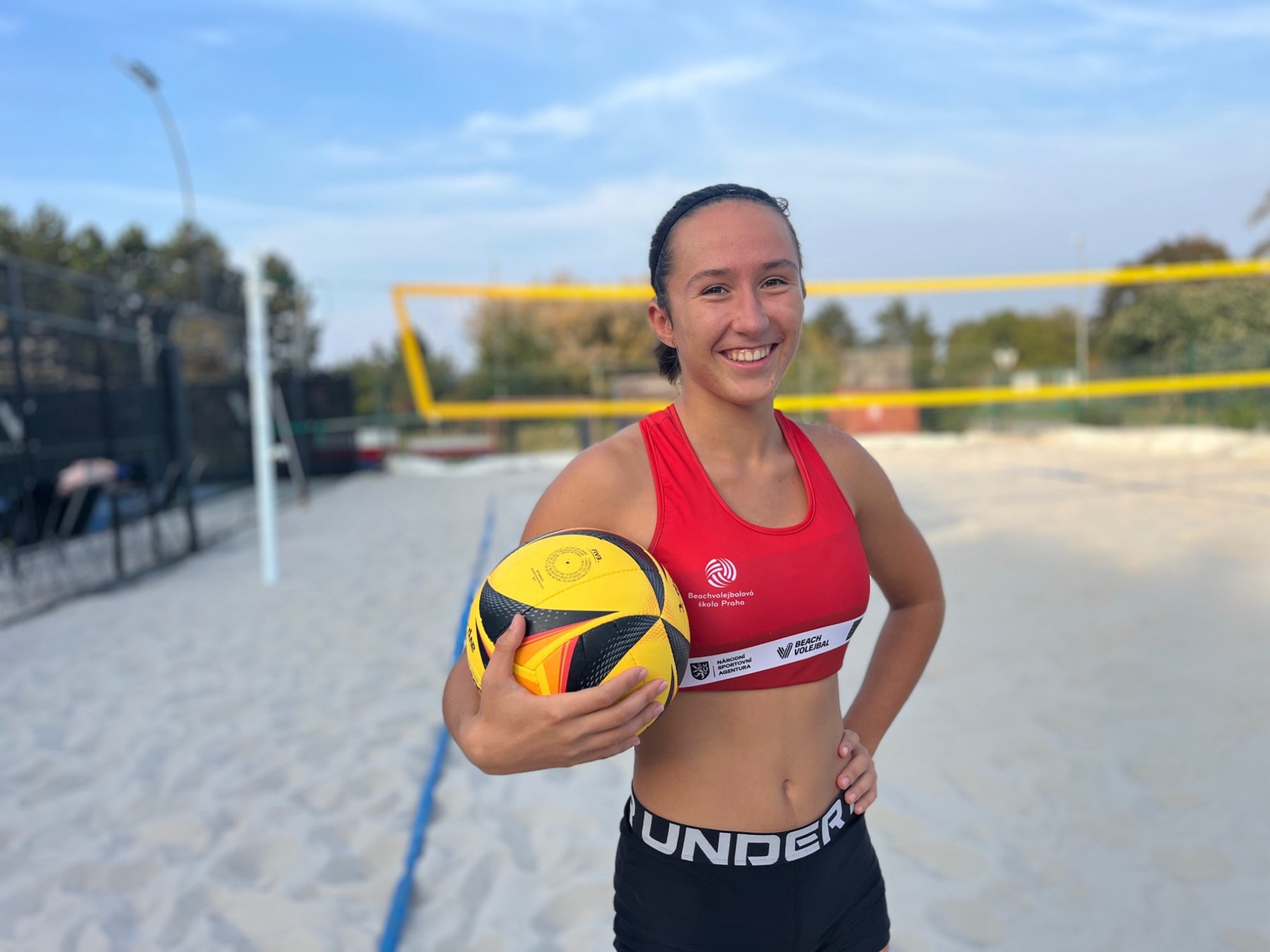 Denisa Černá in a red beach volleyball jersey, holding a ball